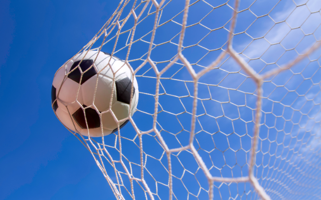 ballon de foot s'écrasant dans le filet lors d'un but, avec en fond un ciel bleu