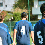 5 membres de l'équipe de foot de l'ESB Bruges qui marchent de dos, le dernier 3/4 face