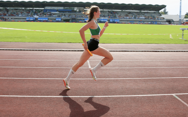 Jeune femme qui court sure une piste d'athlétisme, relais à la main