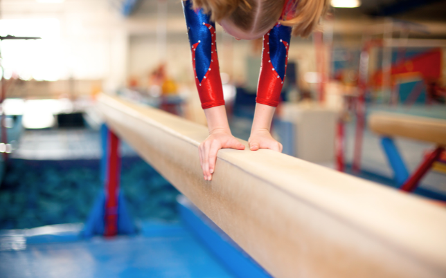 Petite fille faisant le piquet sur une poutre d'agrès pour la gym sportive